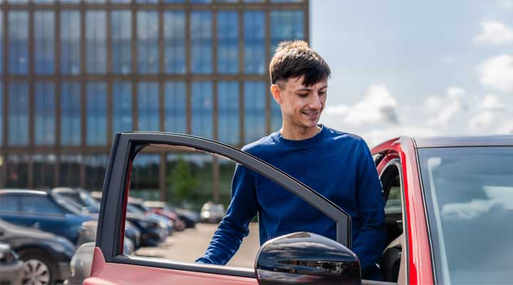 young person getting into the car in front of urban building.