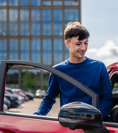 young person getting into the car in front of urban building.