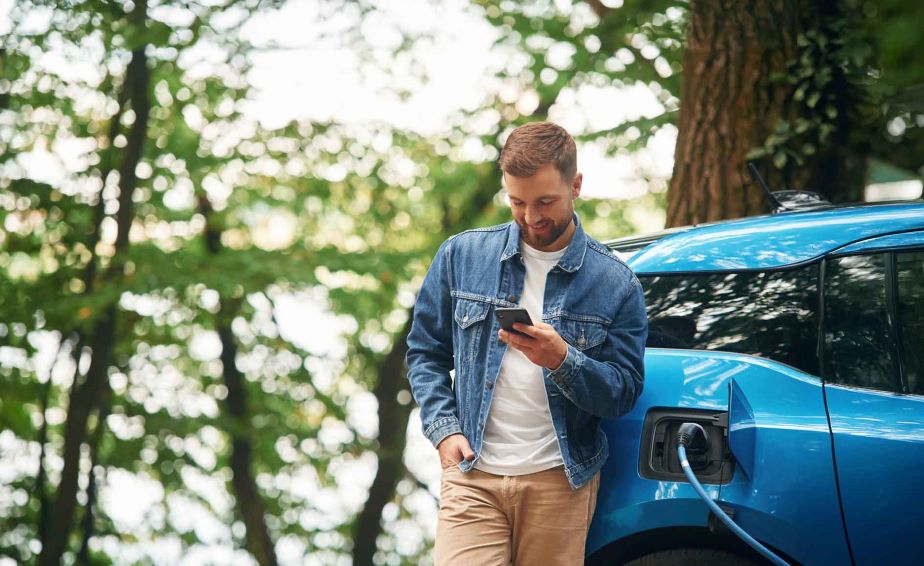 Person standing in front of charged car looking at phone app.