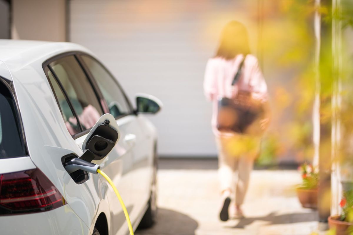 Car charging at home charge point whilst person is walking away into their home for the evening.